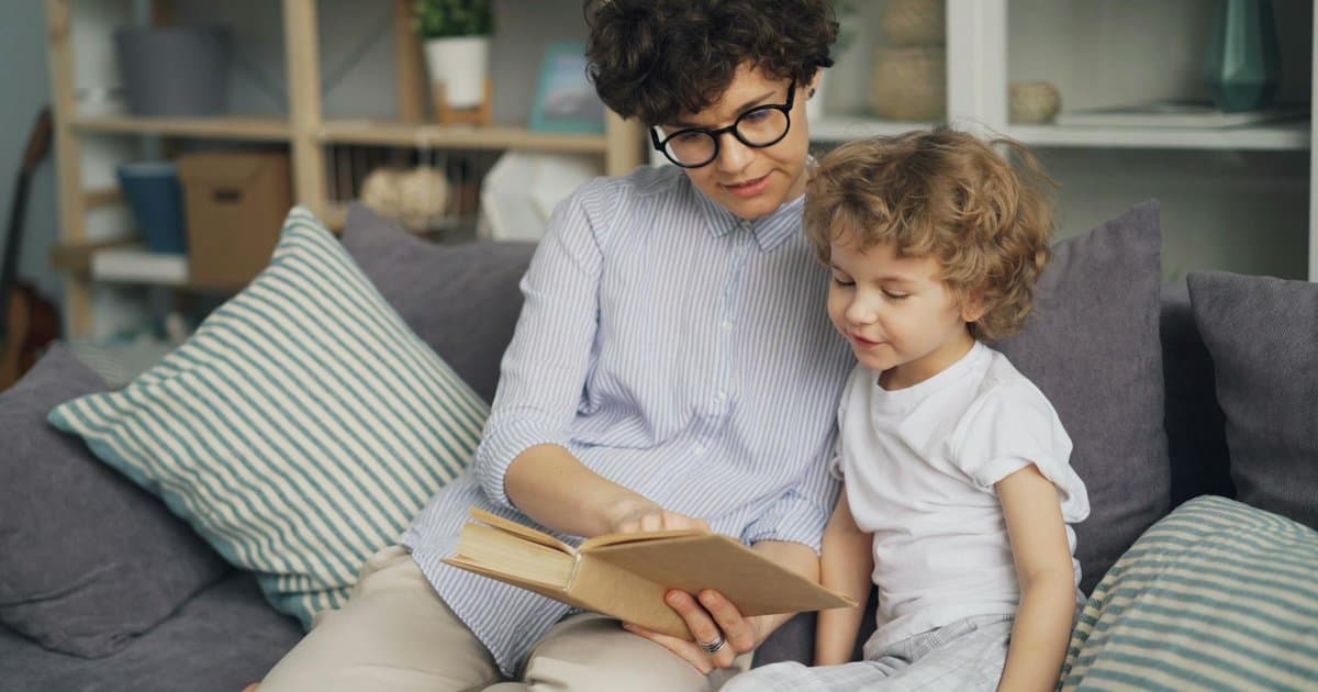 A mother and young son read together on a couch, comparing personalized children's books.